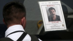 A Federal Police officer stands next to a patrol car with a picture of fugitive drug lord Joaquin "El Chapo" Guzman's on its window, in Acapulco, Guerrero State, Mexico, on July 14, 2015. Mexico's government offered a $3.8 million reward for the capture of "El Chapo" Guzman on Monday and sacked top prison officials amid suspicions that guards helped him escape. Guzman vanished from his cell late Saturday even though he was wearing a monitoring bracelet and surveillance cameras were trained on the room 24 hours a day, Interior Minister Miguel Angel Osorio Chong said. AFP PHOTO / PEDRO PARDO        (Photo credit should read Pedro PARDO/AFP/Getty Images)